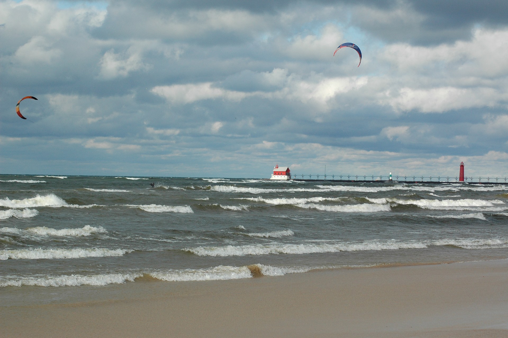 Two kiteboarders riding in whitecaps off Grand Haven City Beach with the pierhead lighthouse behind