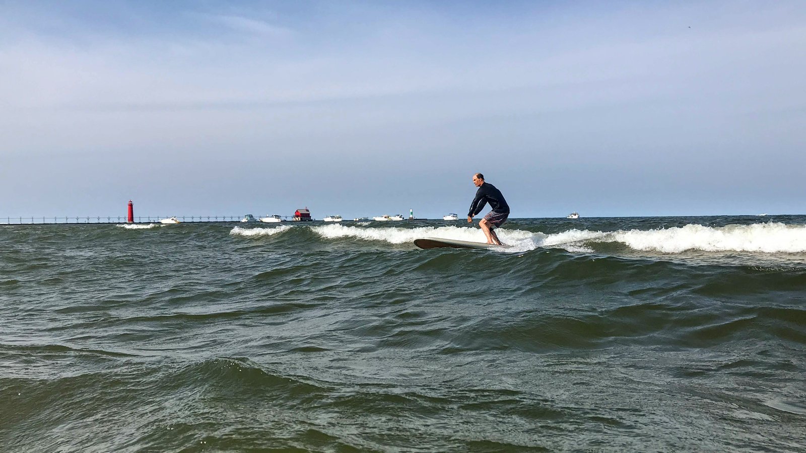 Surfer riding a south-wind wave on the north side at Grand Haven, with the pierhead light behind
